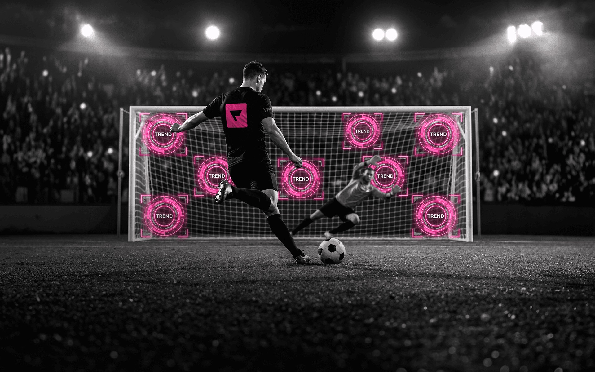Jogador cobrando um pênalti em estádio noturno, com alvos rosa marcados no gol.