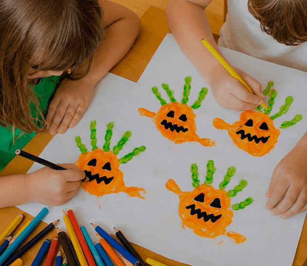 Crianças desenhando monstrinhos numa folha, transformando carimbos de mão em personagens laranja.