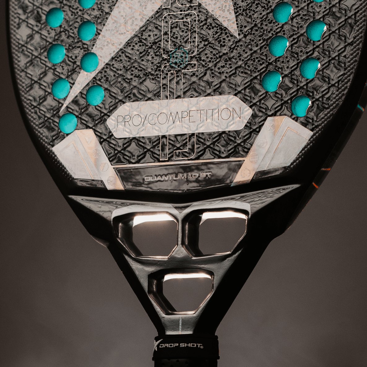Raquete de beach tennis Drop Shot Quantum 1.0 BT, face preta com detalhes turquesa, segurada pelo cabo.