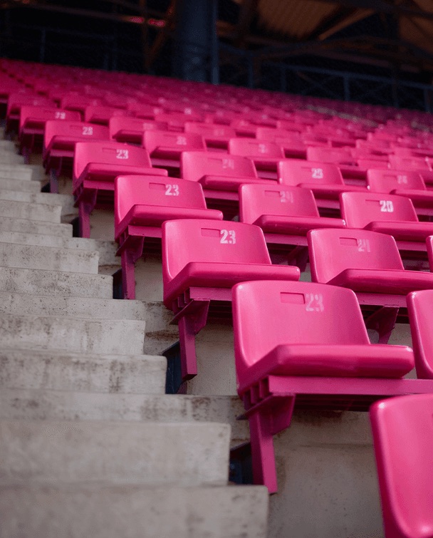 Fileiras de cadeiras rosa vazias na arquibancada de um estádio, vistas de lado.
