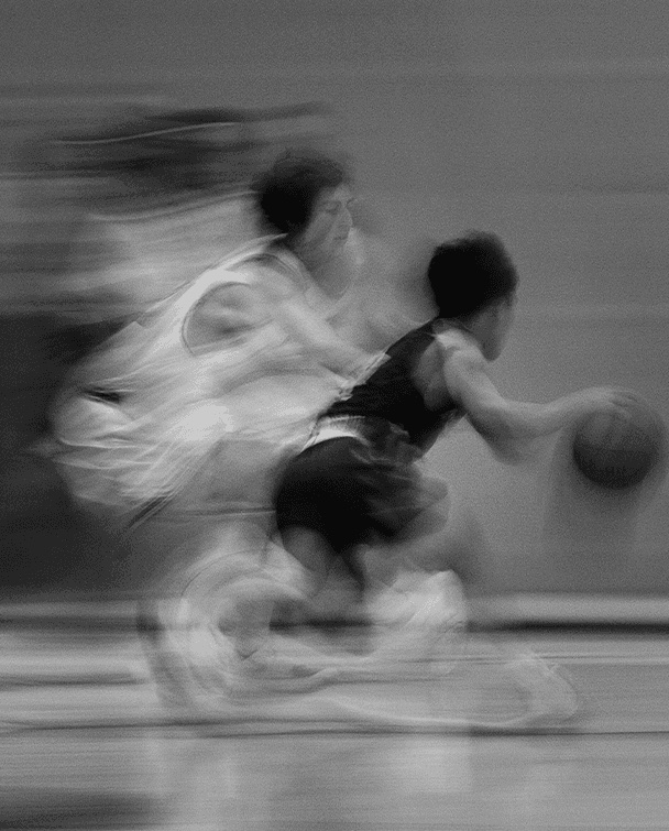 Dois jogadores de basquete em disputa de bola, registrados em preto e branco com borrão de movimento.