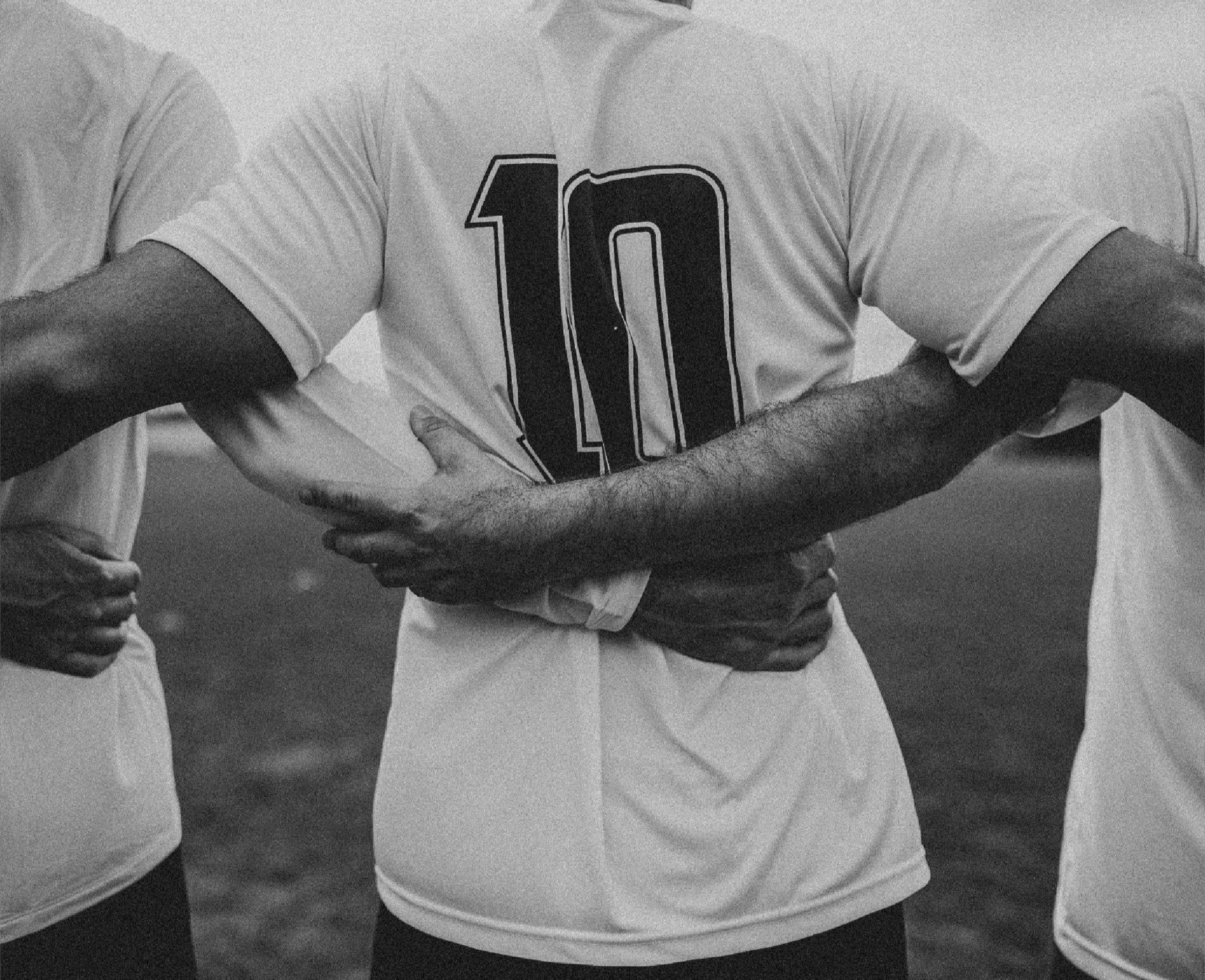 Três jogadores de braços dados, de costas, antes da partida - a camisa do meio traz o número 10.
