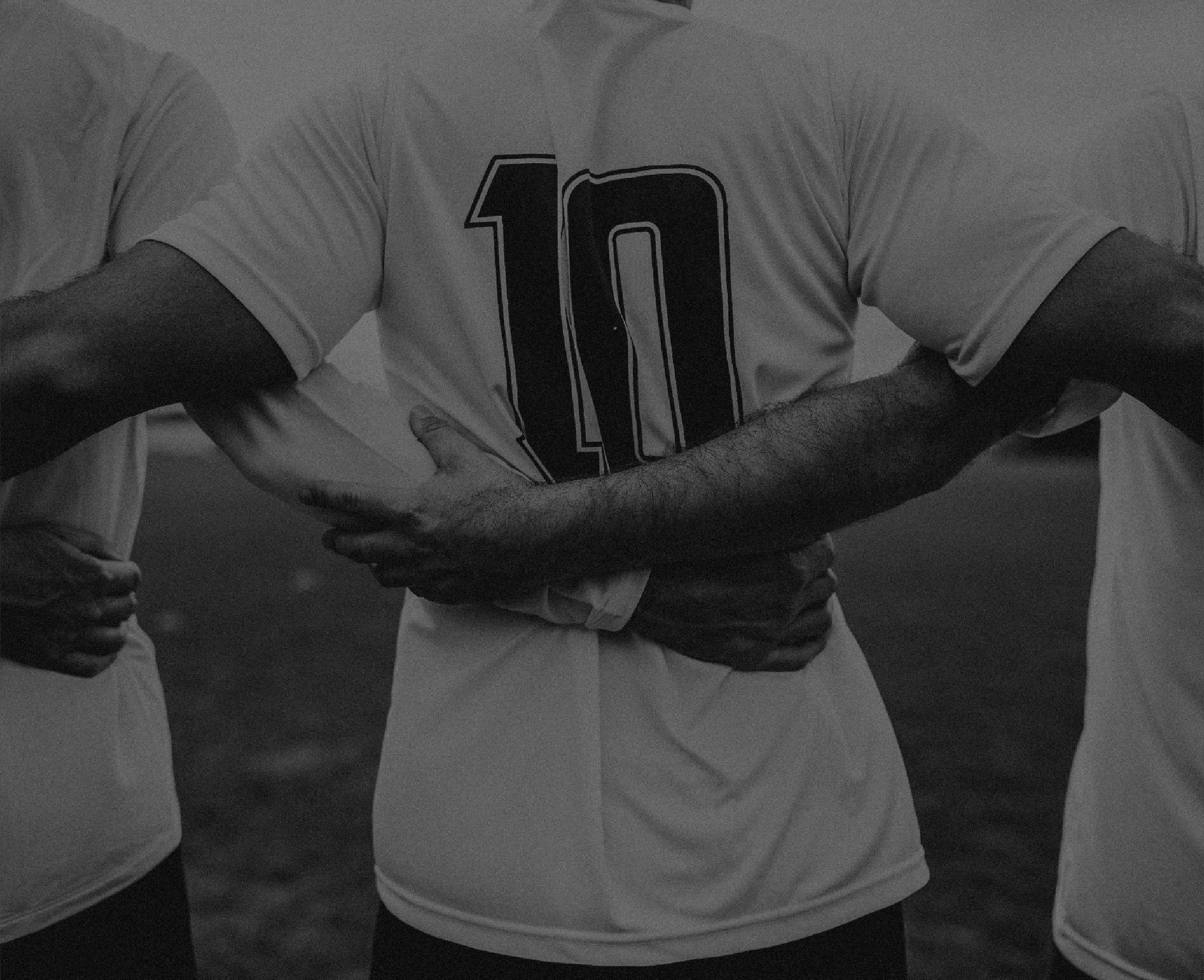 Três jogadores de braços dados, de costas, com a camisa 10 no centro - foto em preto e branco.