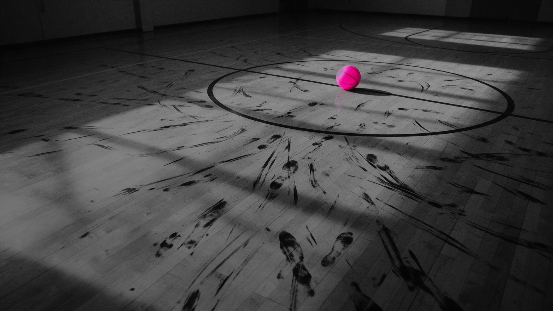 Quadra de basquete vazia depois do jogo: marcas de tênis no piso convergem para uma bola rosa no círculo central, foto em preto e branco.
