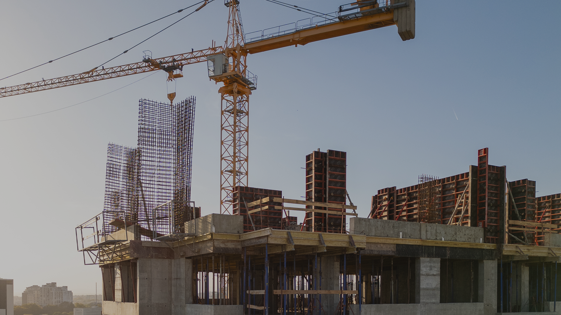 Canteiro de obras do empreendimento ao entardecer: guindaste amarelo sobre a estrutura de concreto, formas de pilares e armaduras de ferro no último pavimento executado.