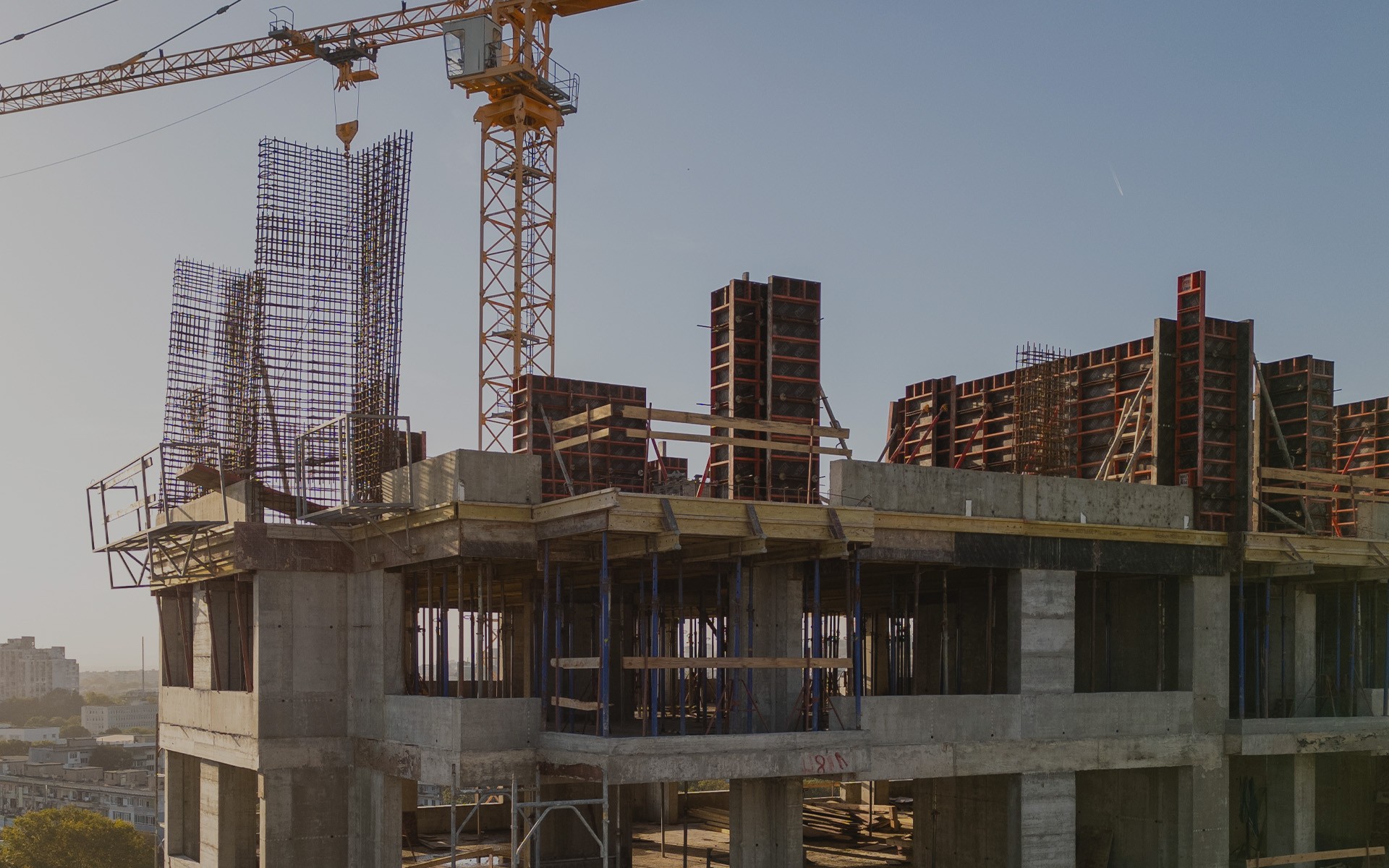 Canteiro de obras do empreendimento ao entardecer: guindaste amarelo sobre a estrutura de concreto, formas de pilares e armaduras de ferro no último pavimento executado.
